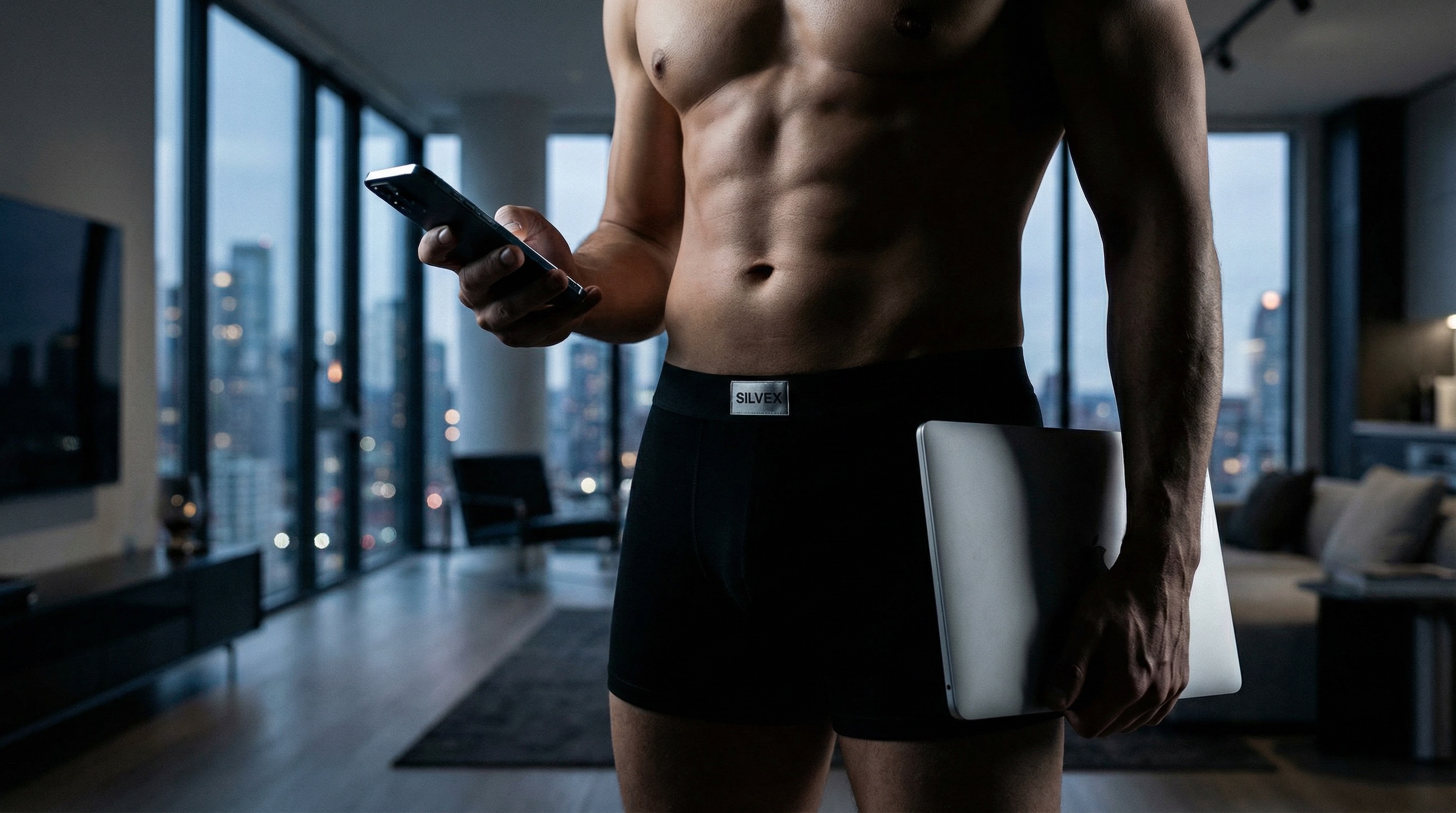 Man wearing SILVEX underwear holding phone and laptop